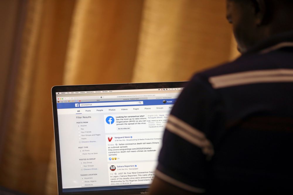 A man, turning his back, opens a Facebook page on his computer to fact check coronavirus disease (COVID-19) information