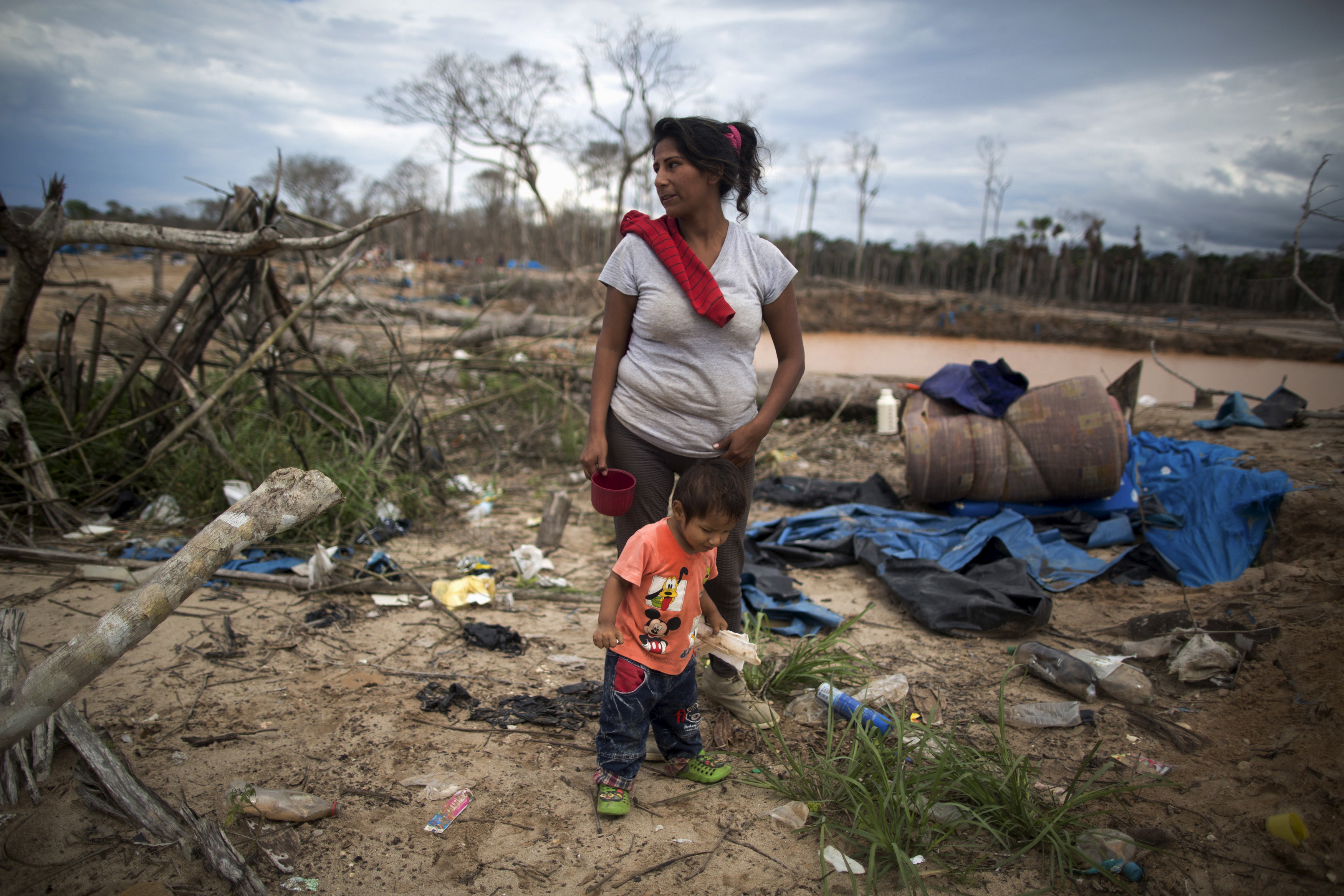 A woman and her child stand near debris after a police operation to destroy illegal gold mining camps in La Pampa, in the southern Amazon region of Madre de Dios, Peru August 11, 2015. REUTERS/Sebastian Castaneda