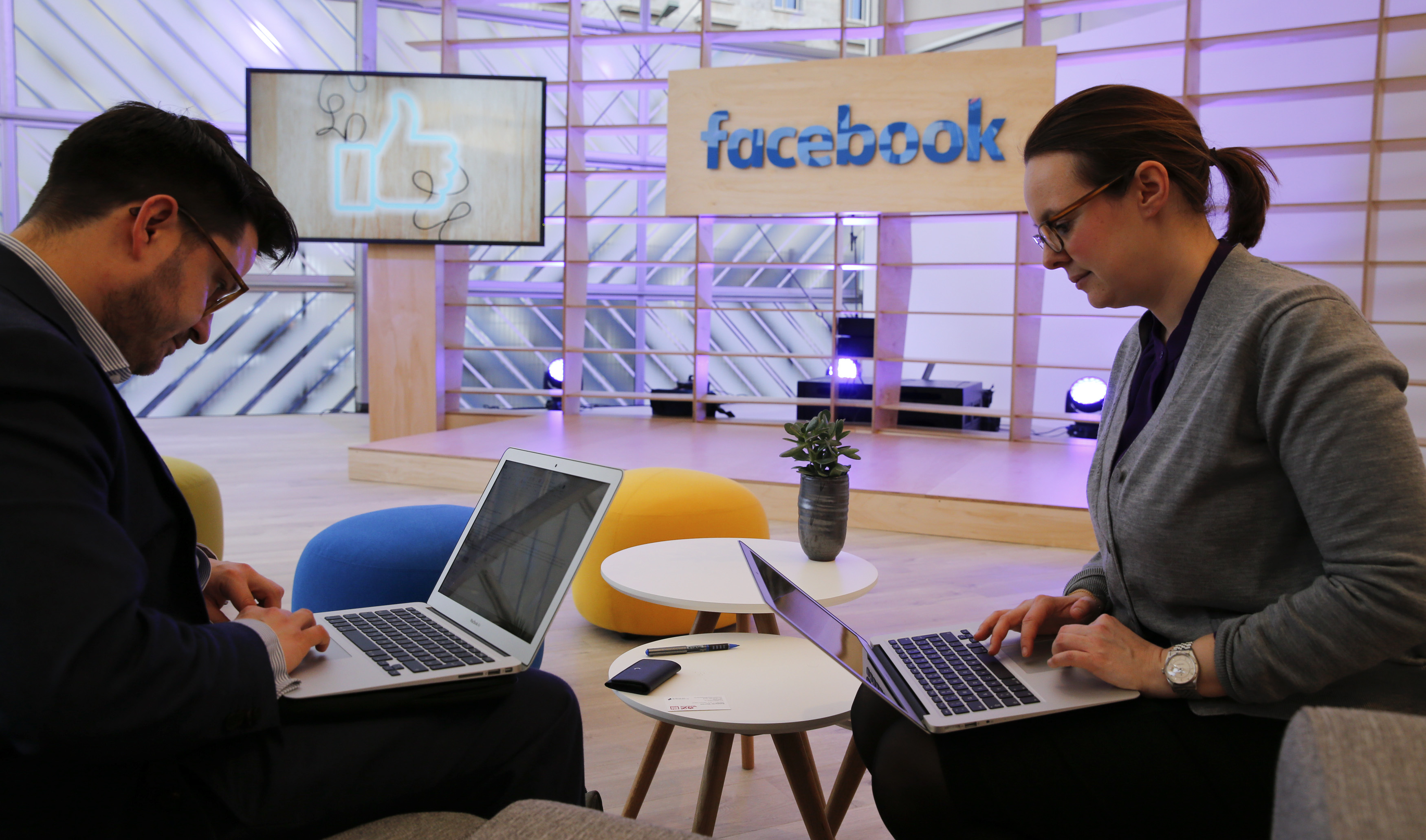 People work with their laptops in front of the Facebook logo at the new Facebook Innovation Hub during a preview media tour in Berlin, Germany, February 24, 2016. REUTERS/Fabrizio Bensch