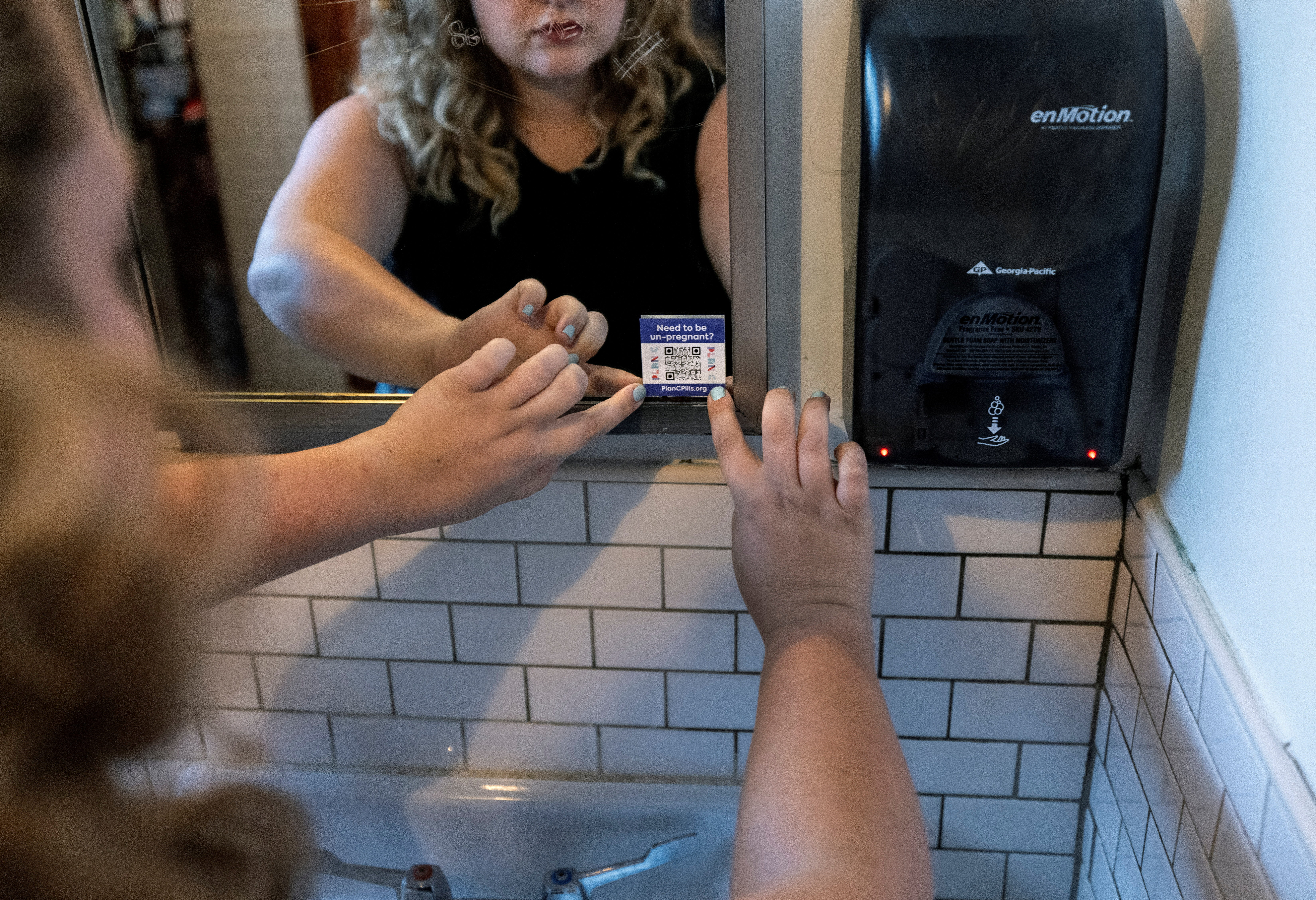 A woman puts stickers in the bathroom of a Houston coffee shop directing people in need of abortions to Plan C, an organization which guides those seeking medical abortions through the process of obtaining abortion inducing medication online, in Texas, U.S., October 1, 2021. REUTERS/Evelyn Hockstein