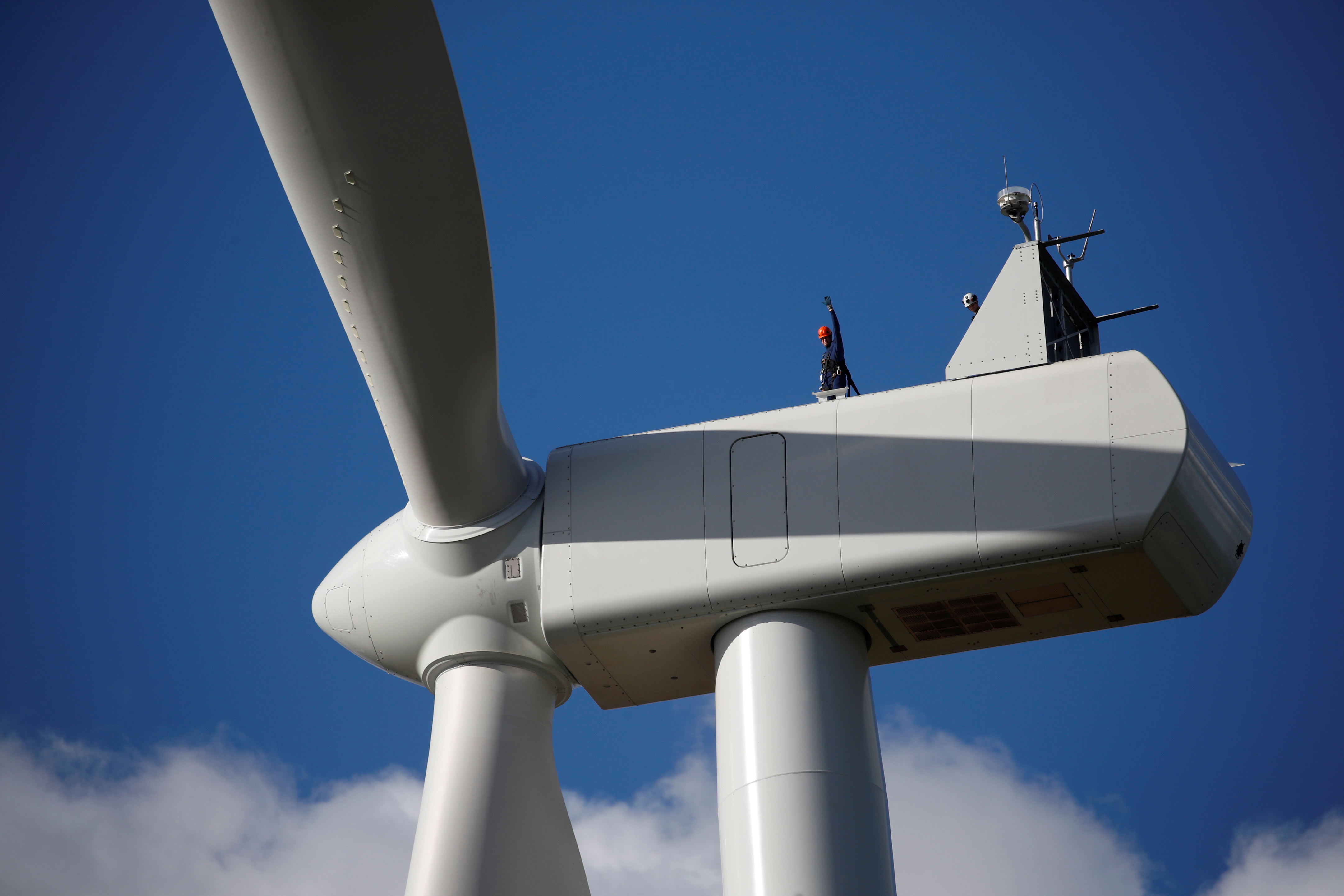 A man waves as he stands on top of a power-generating windmill turbine at the Saint-Pere Energies wind farm in Saint-Pere-en-Retz near Nantes, France, October 22, 2021. REUTERS/Stephane Mahe