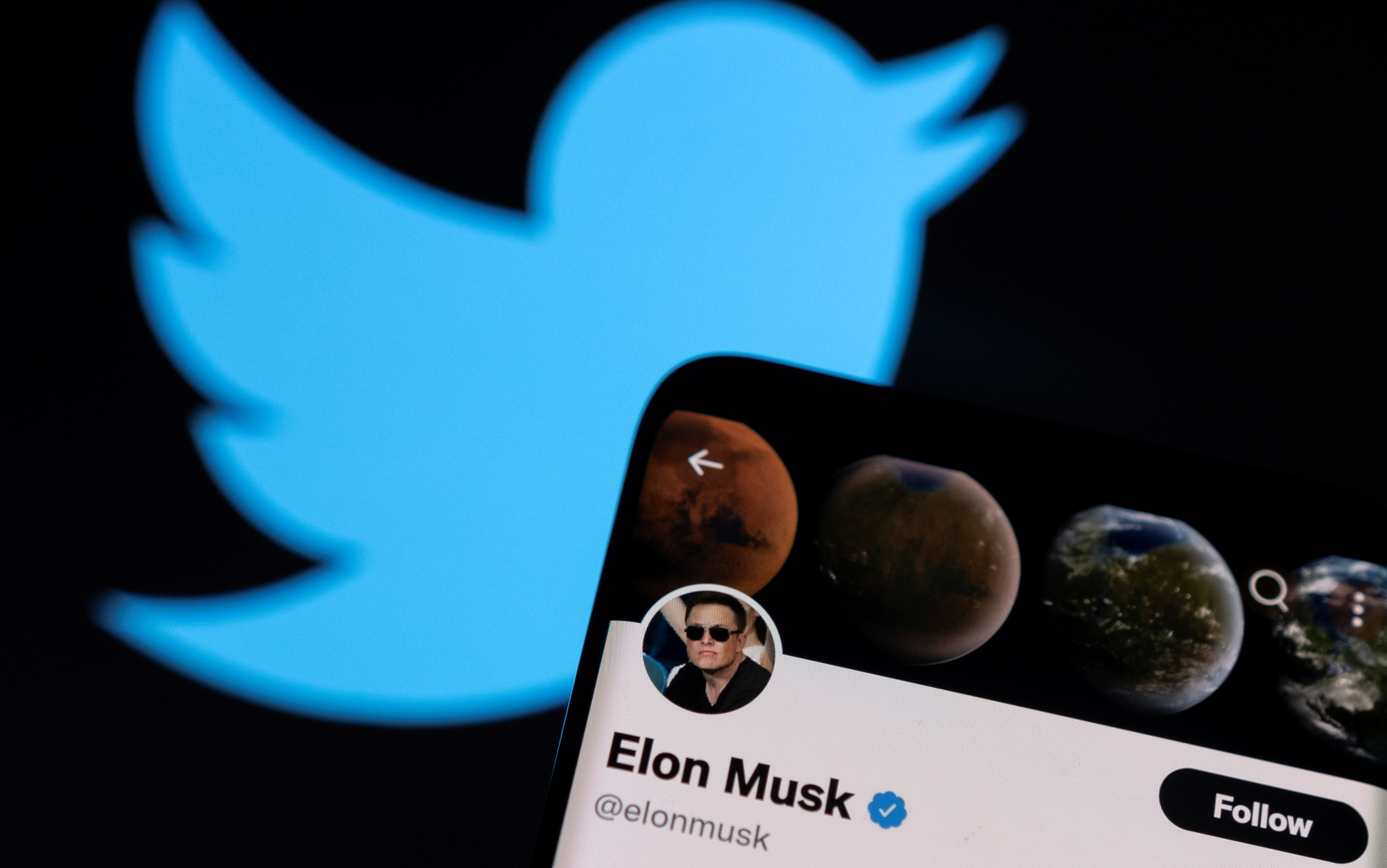 Elon Musk's twitter account is seen on a smartphone in front of the Twitter logo in this photo illustration taken, April 15, 2022