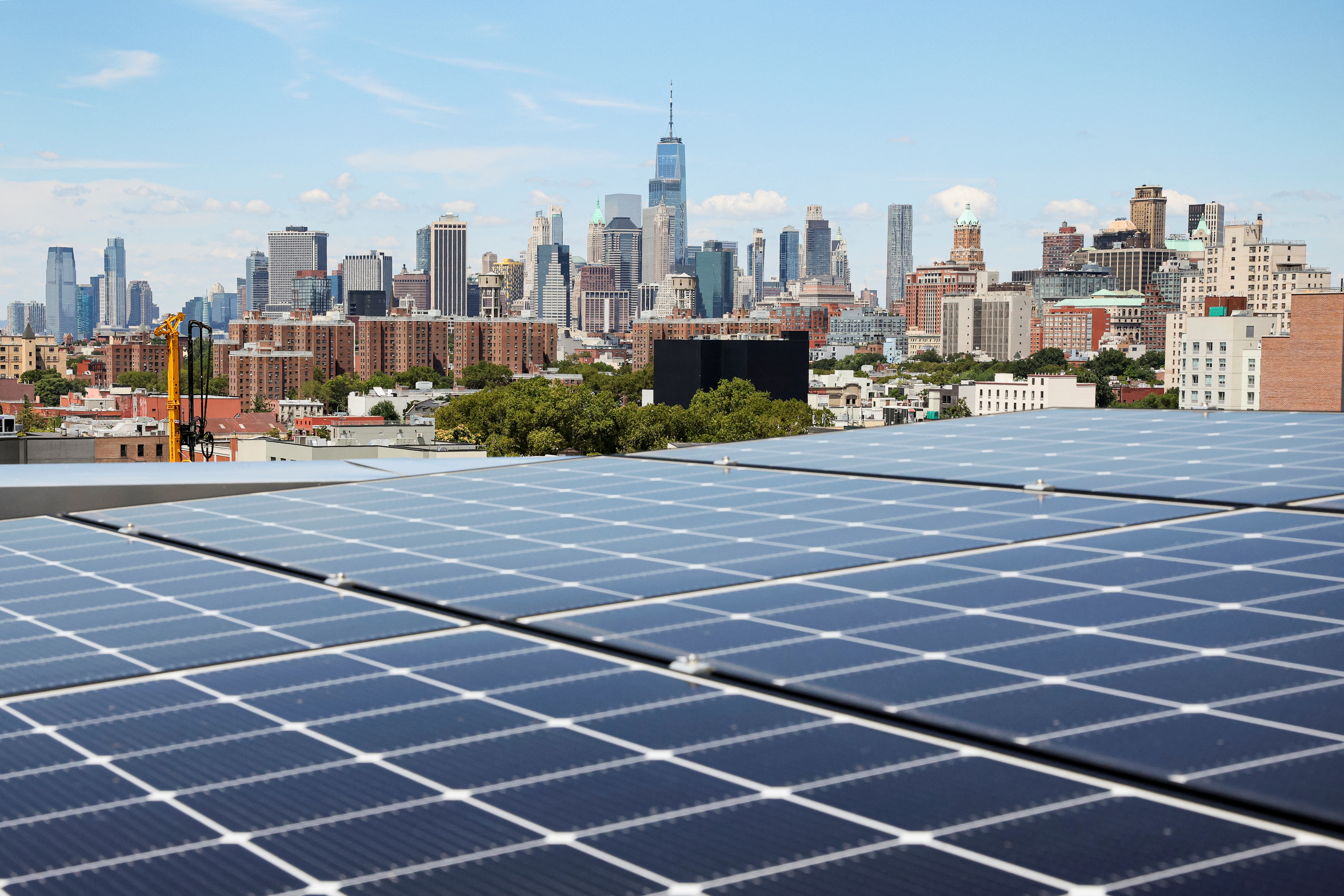 Solar panels are seen along with a view of the neighborhood and lower Manhattan from the rooftop of Timber House, in Brooklyn, New York, U.S., August 16, 2022. REUTERS/Brendan McDermid