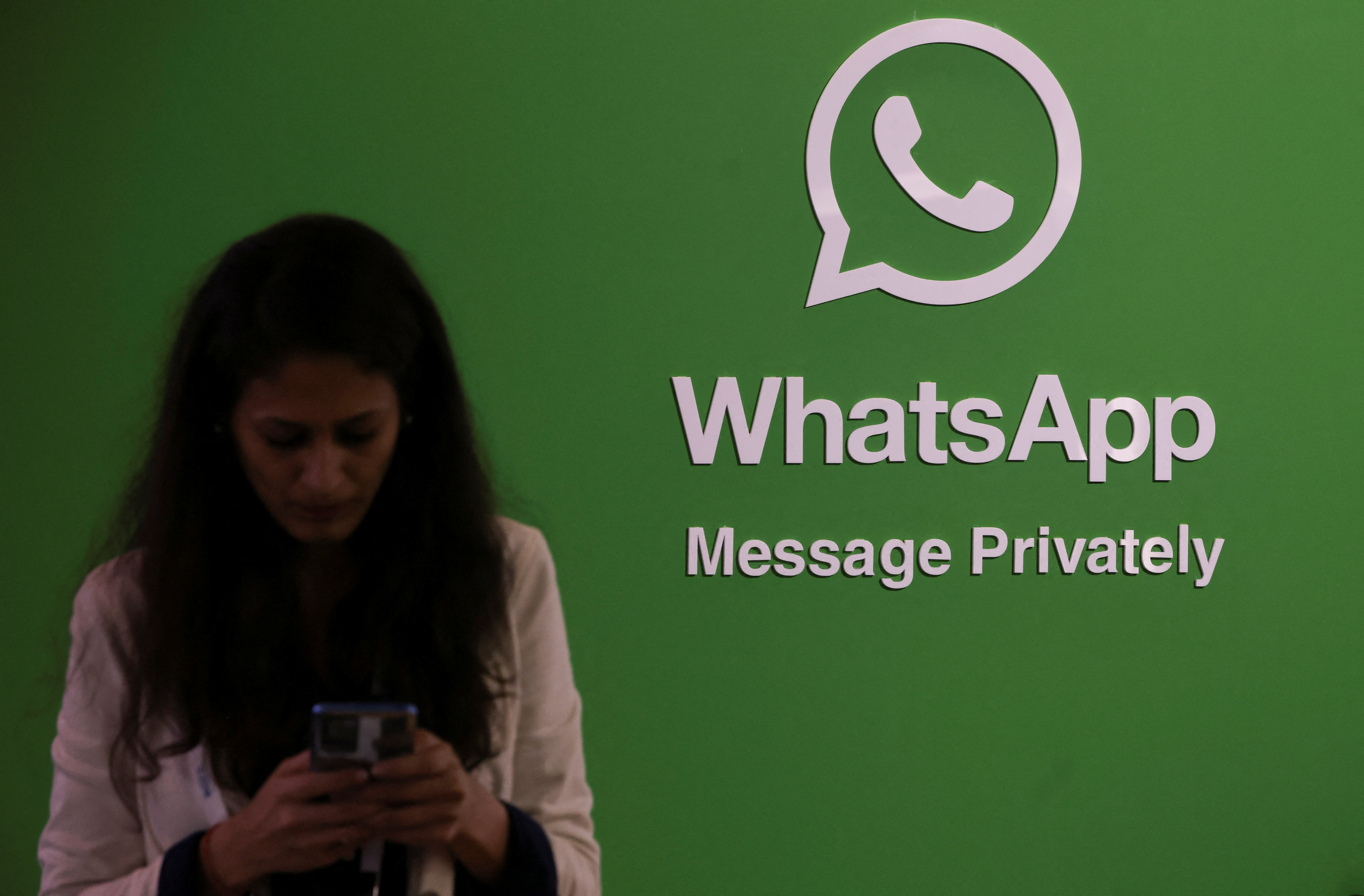 A woman uses her phone next to a logo of the WhatsApp application during Global Fintech Fest in Mumbai, India September 20, 2022