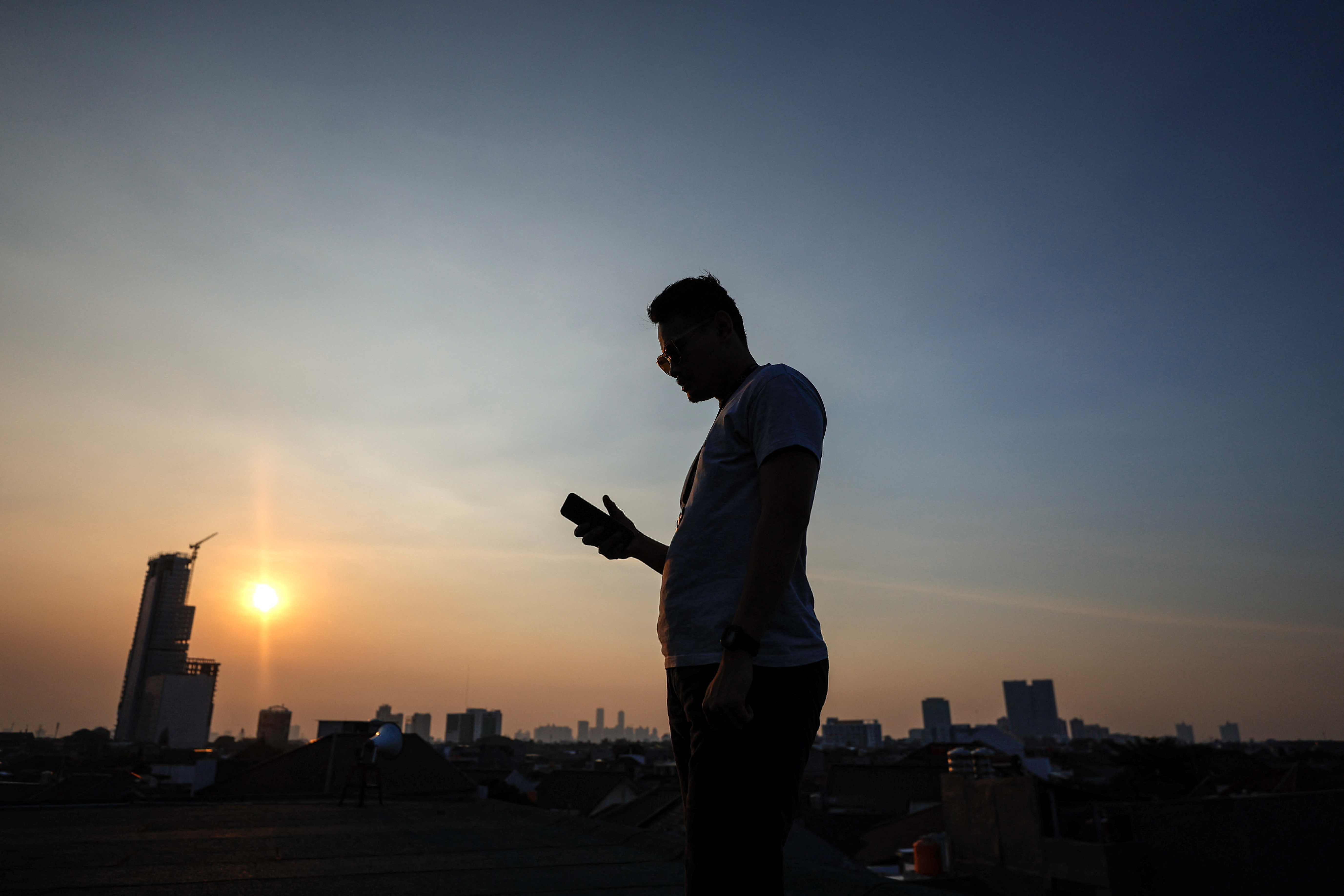 A man uses his mobile phone during sunset in Jakarta, Indonesia, June 11, 2023. REUTERS/Willy Kurniawan