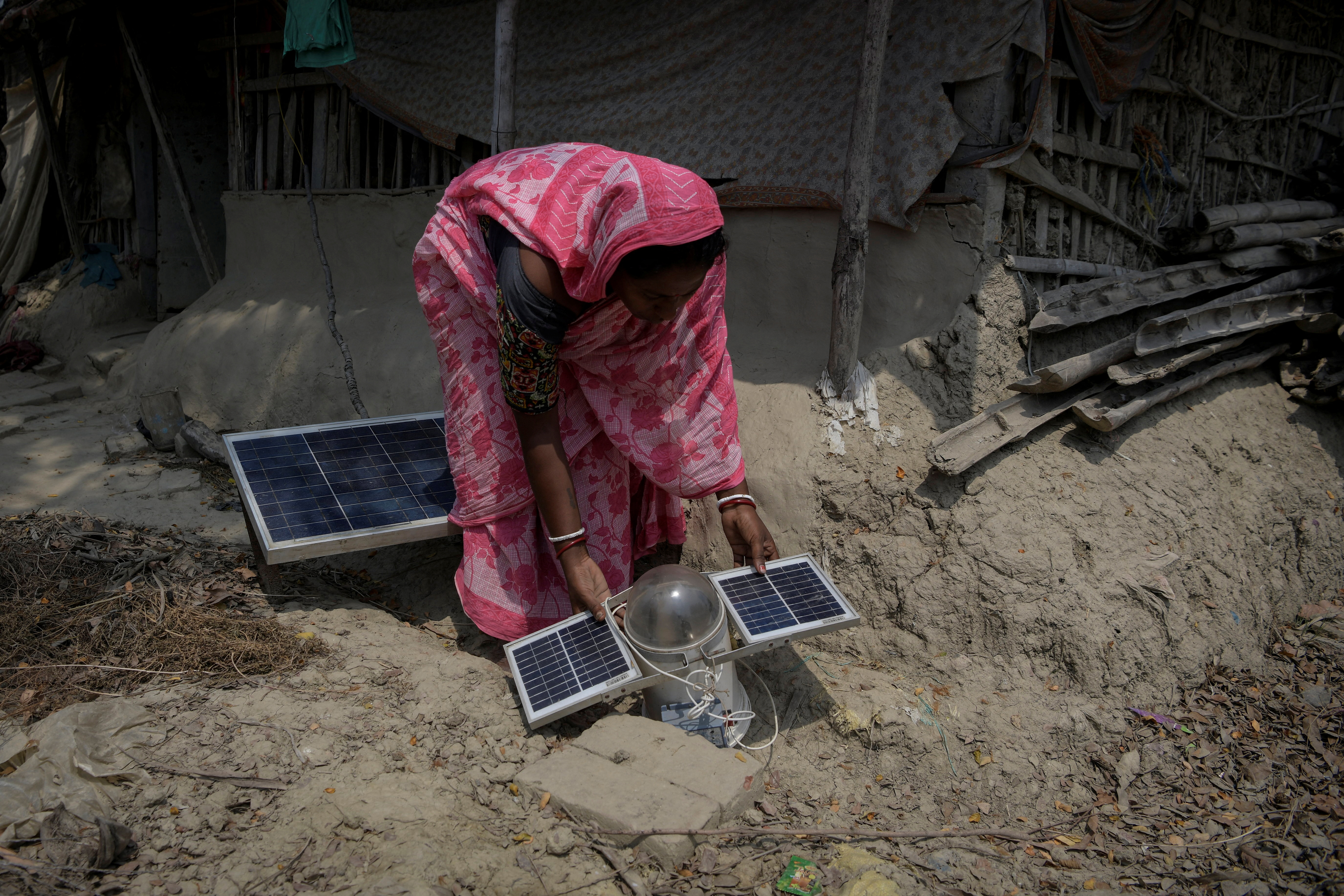 Women places a solar panel light out for charging outside her house on Ghoramara Island in the Sundarbans, West Bengal, India, April 13, 2024. REUTERS/Avijit Ghosh