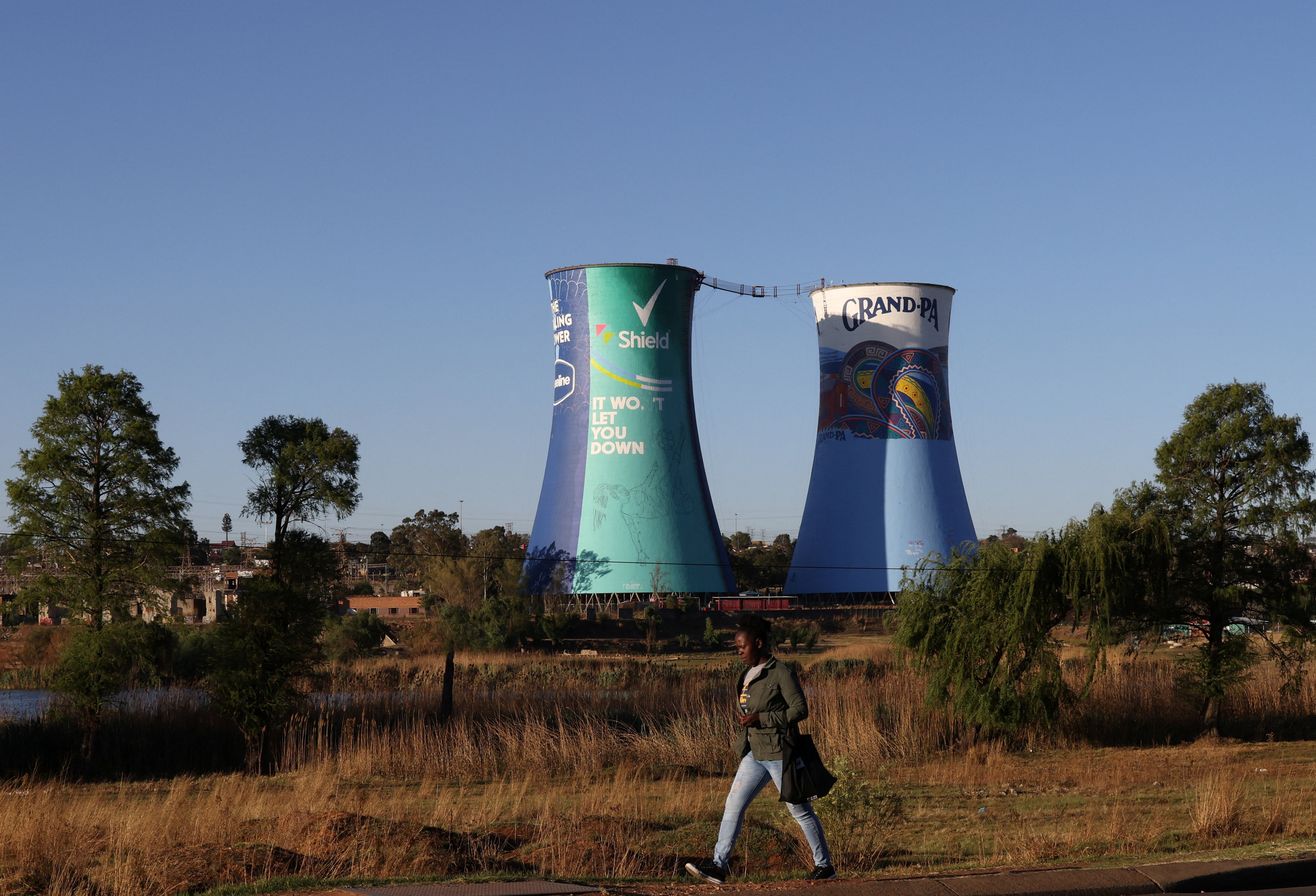 A woman walks past the Orlando Power Station, a decommissioned coal-fired facility now repurposed for bungee jumping between its iconic twin towers, one of the attractions drawing tourists to Soweto, South Africa September 30, 2024. REUTERS/Siphiwe Sibeko