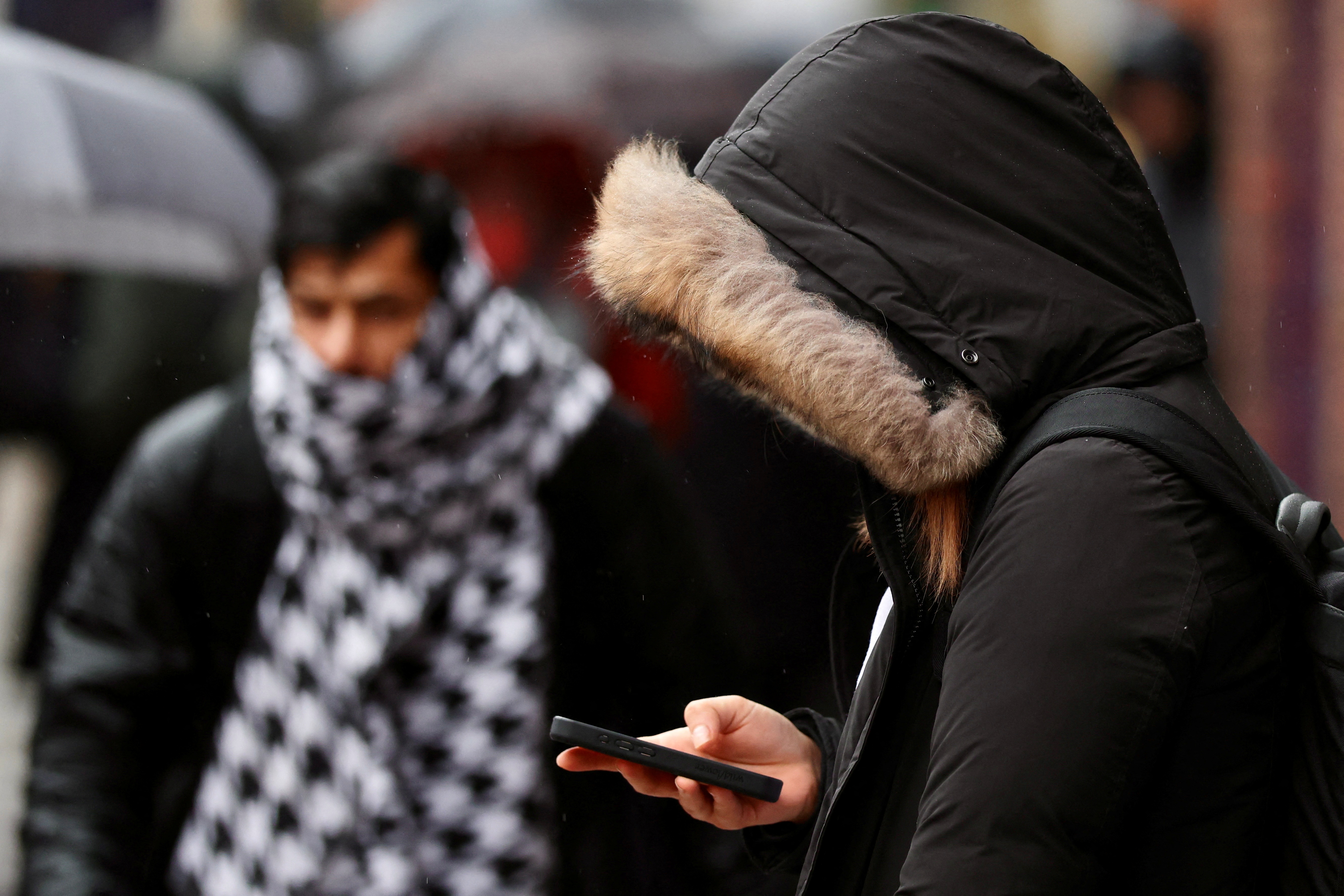 A person wearing a heavy coat looks at a mobile phone  in London, Britain, January 6, 2025. REUTERS/Kevin Coombs