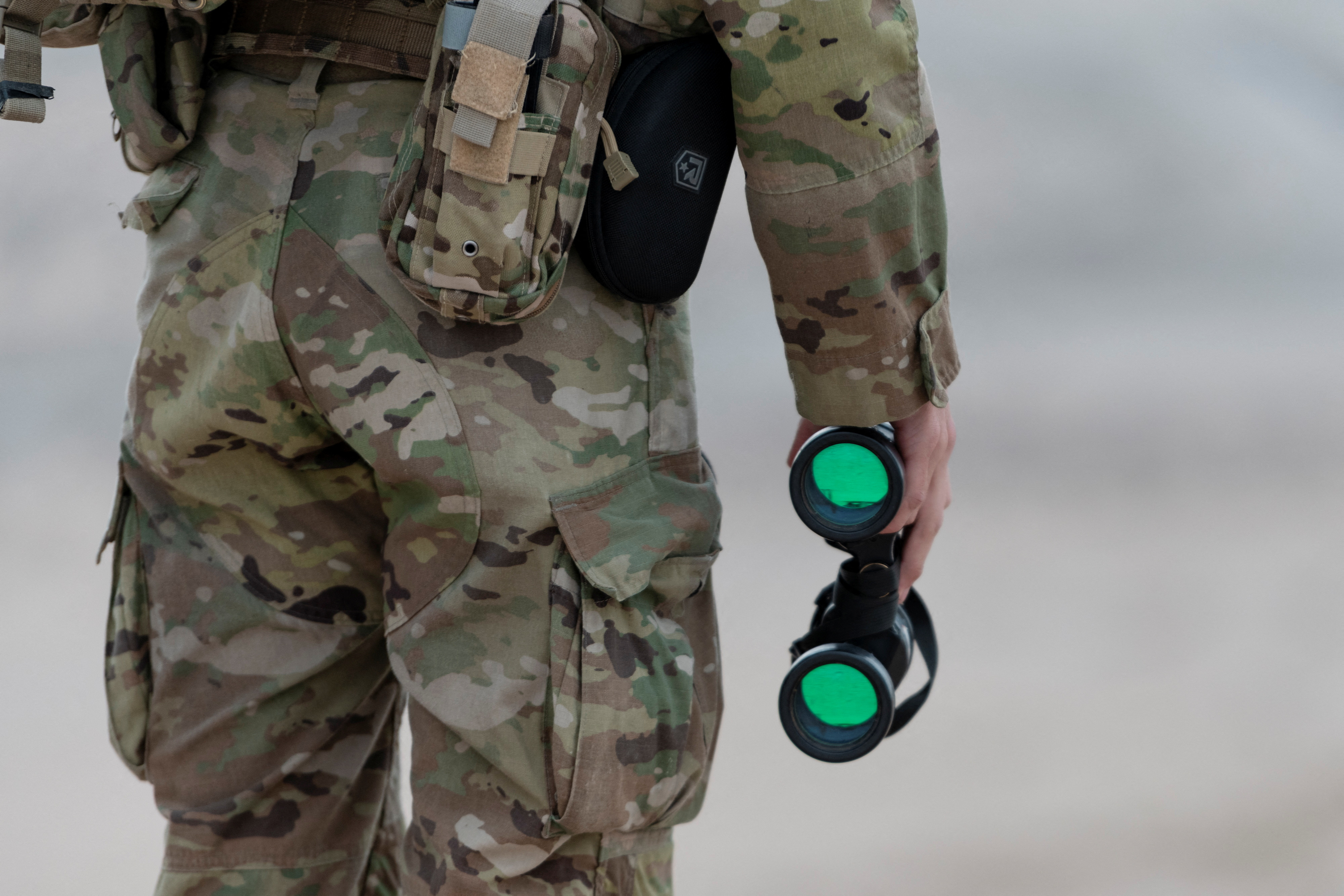 A U.S. National Guardsman holds binoculars while surveilling from a hill overlooking the U.S.-Mexico border in Sunland Park, New Mexico, U.S., March 27, 2025. REUTERS/Cheney Orr