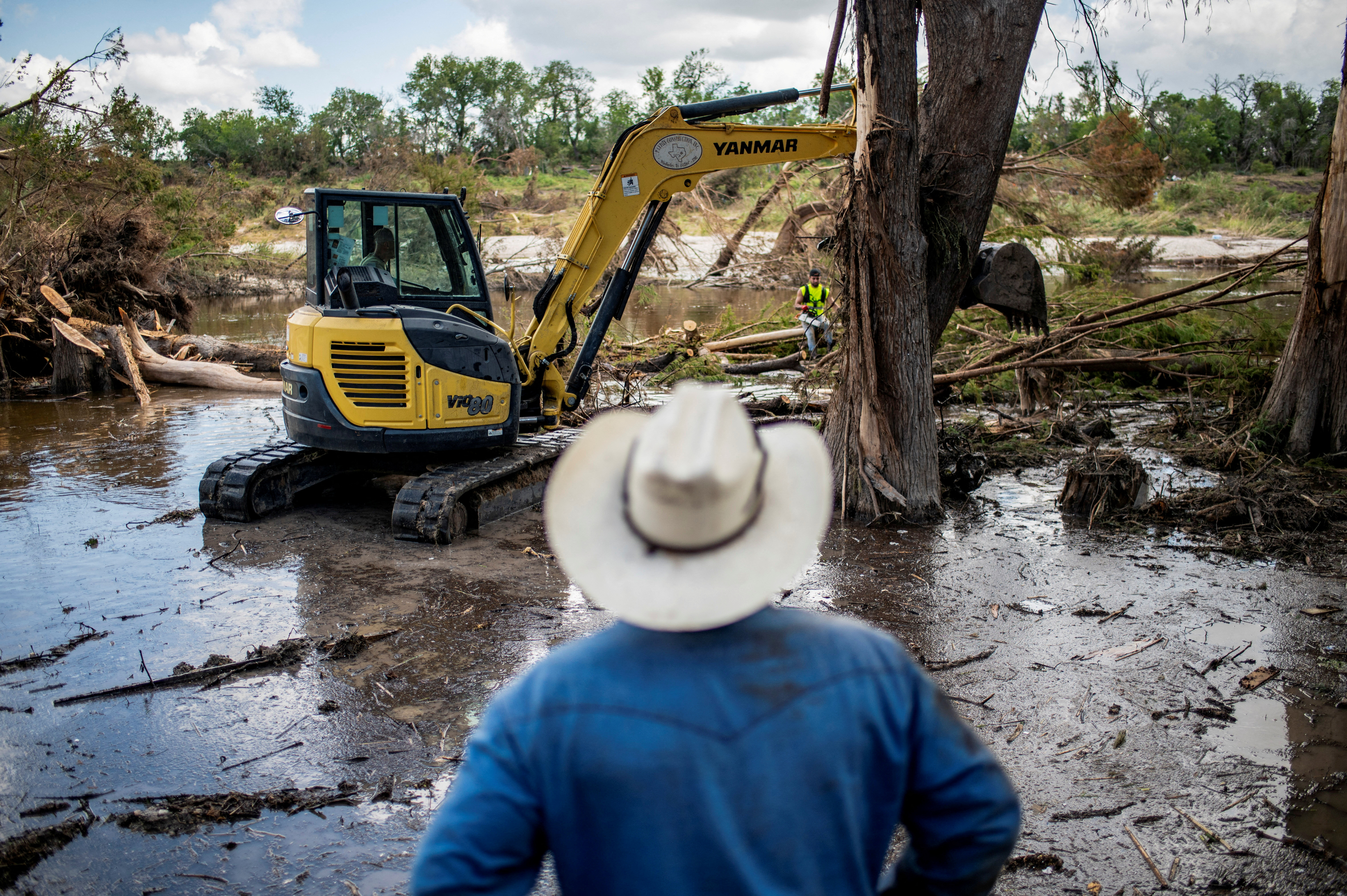 A person watches as machinery is used to clear debris along the banks of the Guadalupe River after catastrophic floods in Center Point, Texas, U.S., July 11, 2025. REUTERS/Sergio Flores