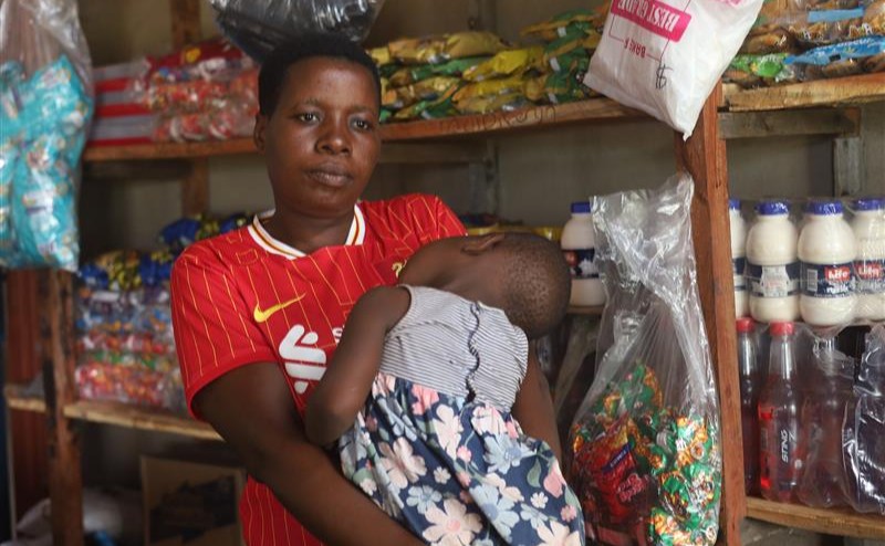 Joyce Chaipa, who lost her job clearing mines in Zimbabwe after U.S. funding cuts, stands with her child inside her shop in Rushinga, Zimbabwe, Dec 7, 2025. Thomson Reuters Foundation/Farai Shawn Matiashe.